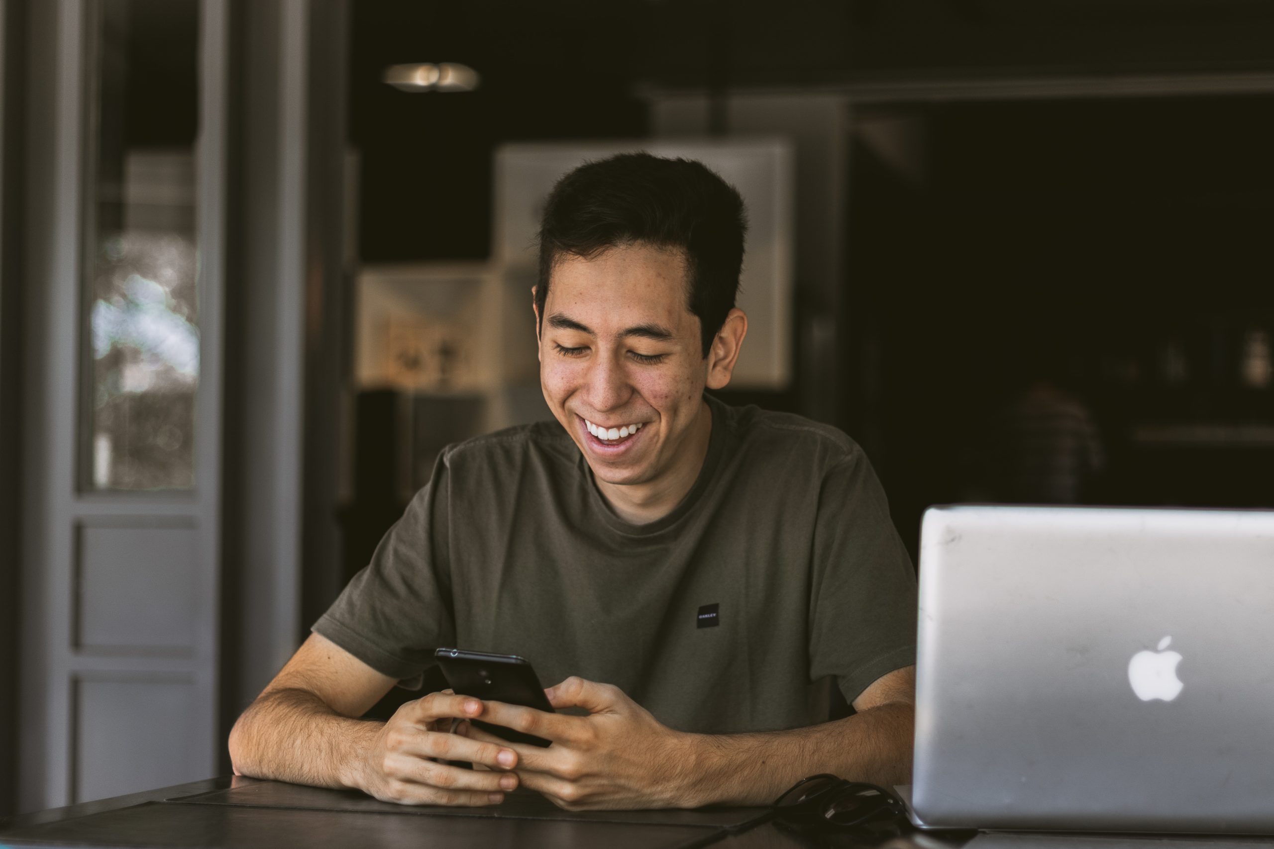 Photo of smiling man with laptop looking at his phone
